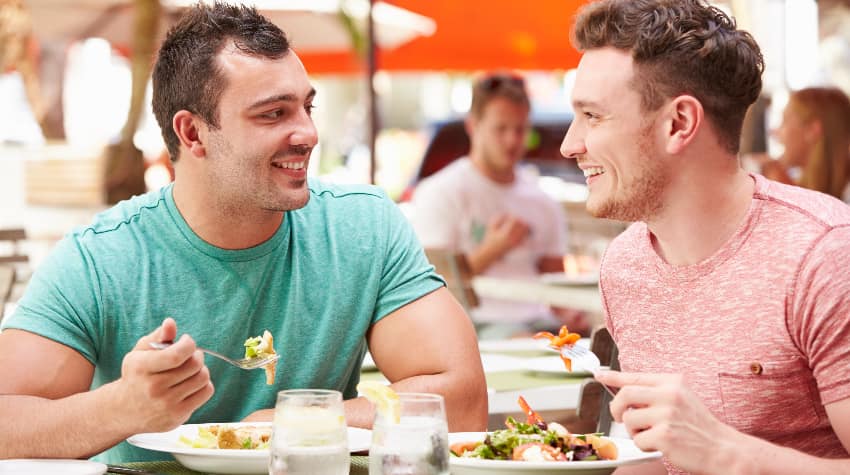 Two men smile and enjoy a meal on an outdoor patio