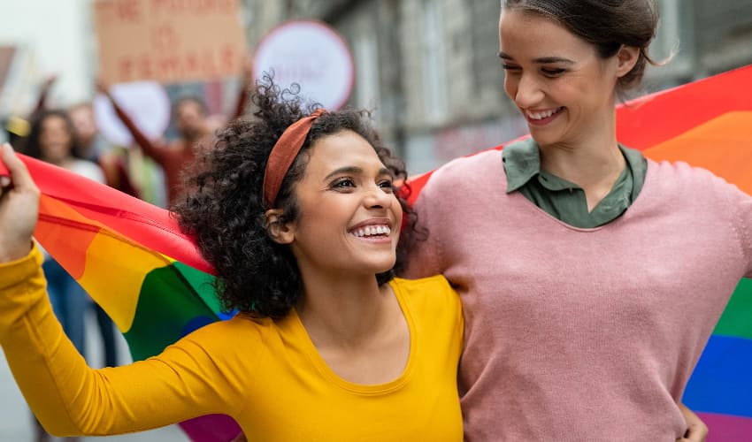 Two women hold a rainbow pride flag and march in a parade