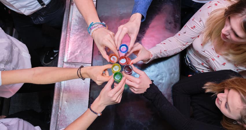 A group of cheers toast a round of rainbow-colored shots at a bar