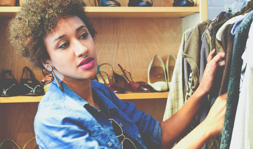 A woman in trendy clothes searches a clothing rack at a thrift store