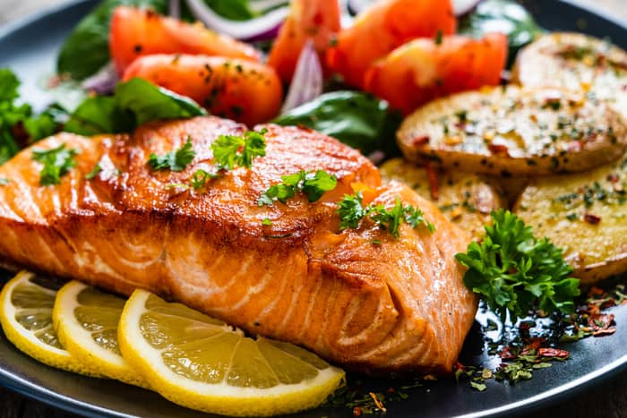 baked salmon over a bed of lemon slices with vegetables in the background