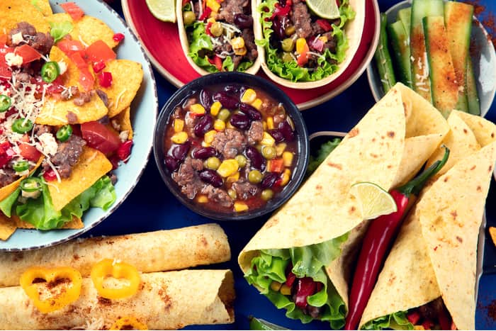 tacos, black beans with corn, lettuce, and other dressings in tortillas arranged on a table