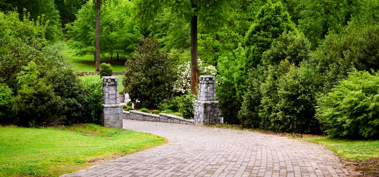 a stone-paved path lined with two stone columns leading into a green area with lots of trees at grant park