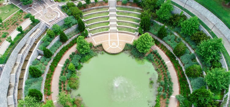 a large circular fountain with green-tinted water surroundd by trees and a pavement