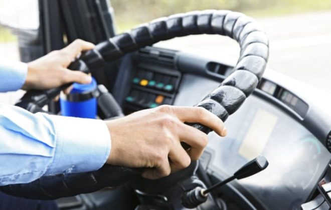 A close up of a bus driver's hands on the wheel