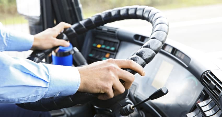 A close up of a bus driver's hands on the wheel