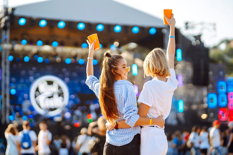 Two women embracing each other and raising drinks in the air at a concert